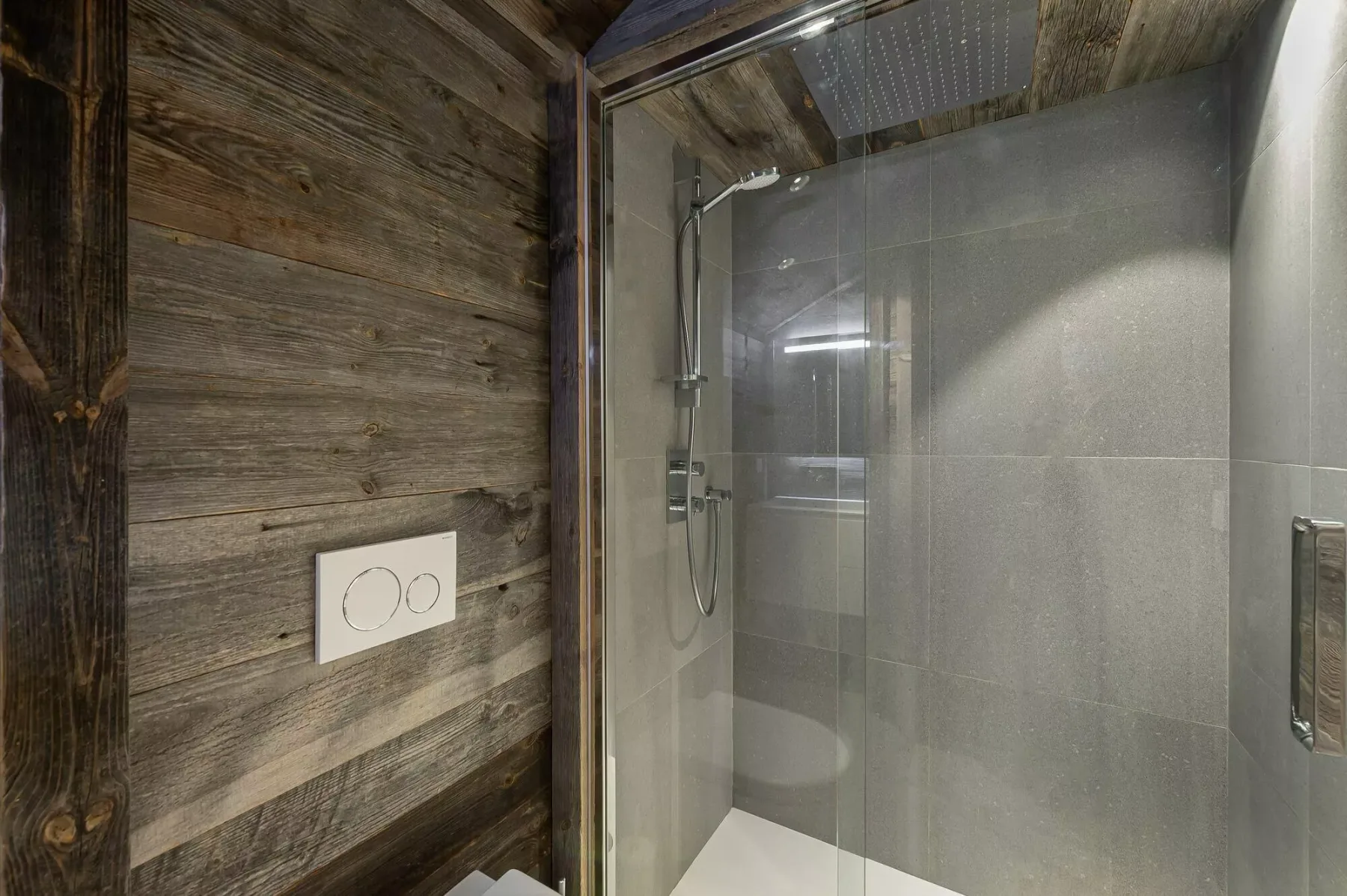 A tiled shower with a glass panel beside a wood-paneled wall.