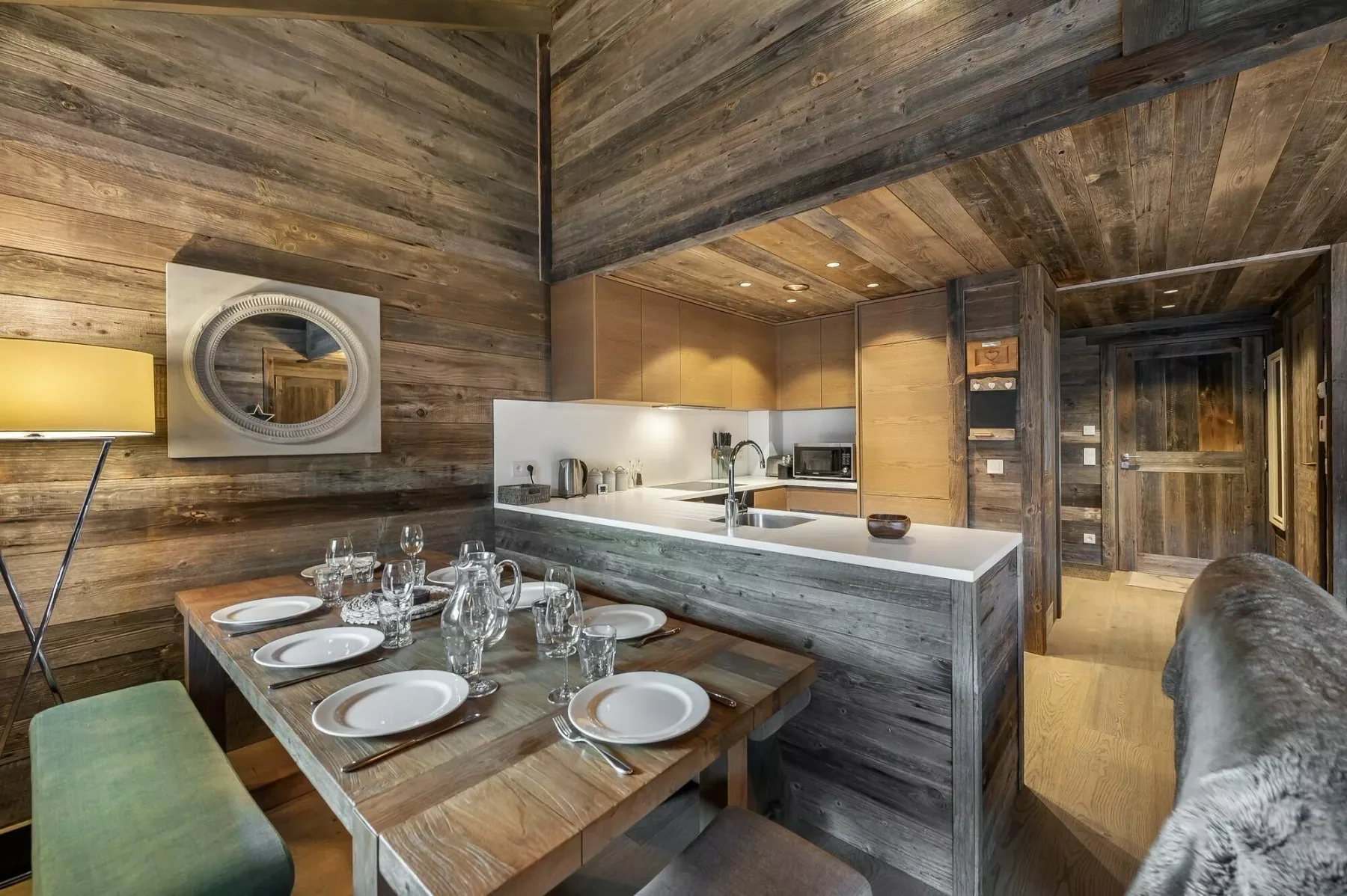 A rustic dining area beside a compact kitchen, with a set table and wood-paneled walls.