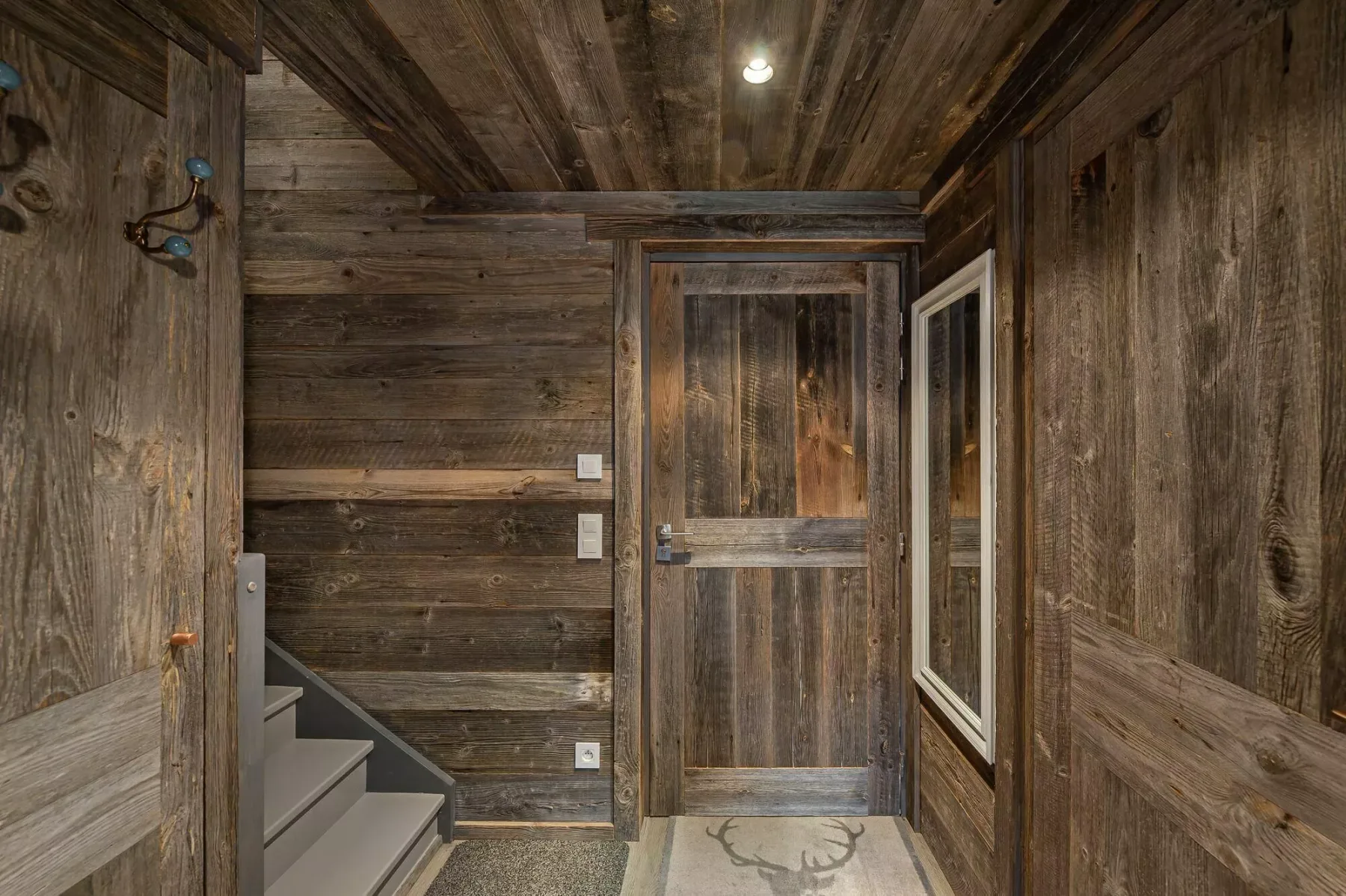 A rustic wood-paneled entryway with a staircase and a closed wooden door.