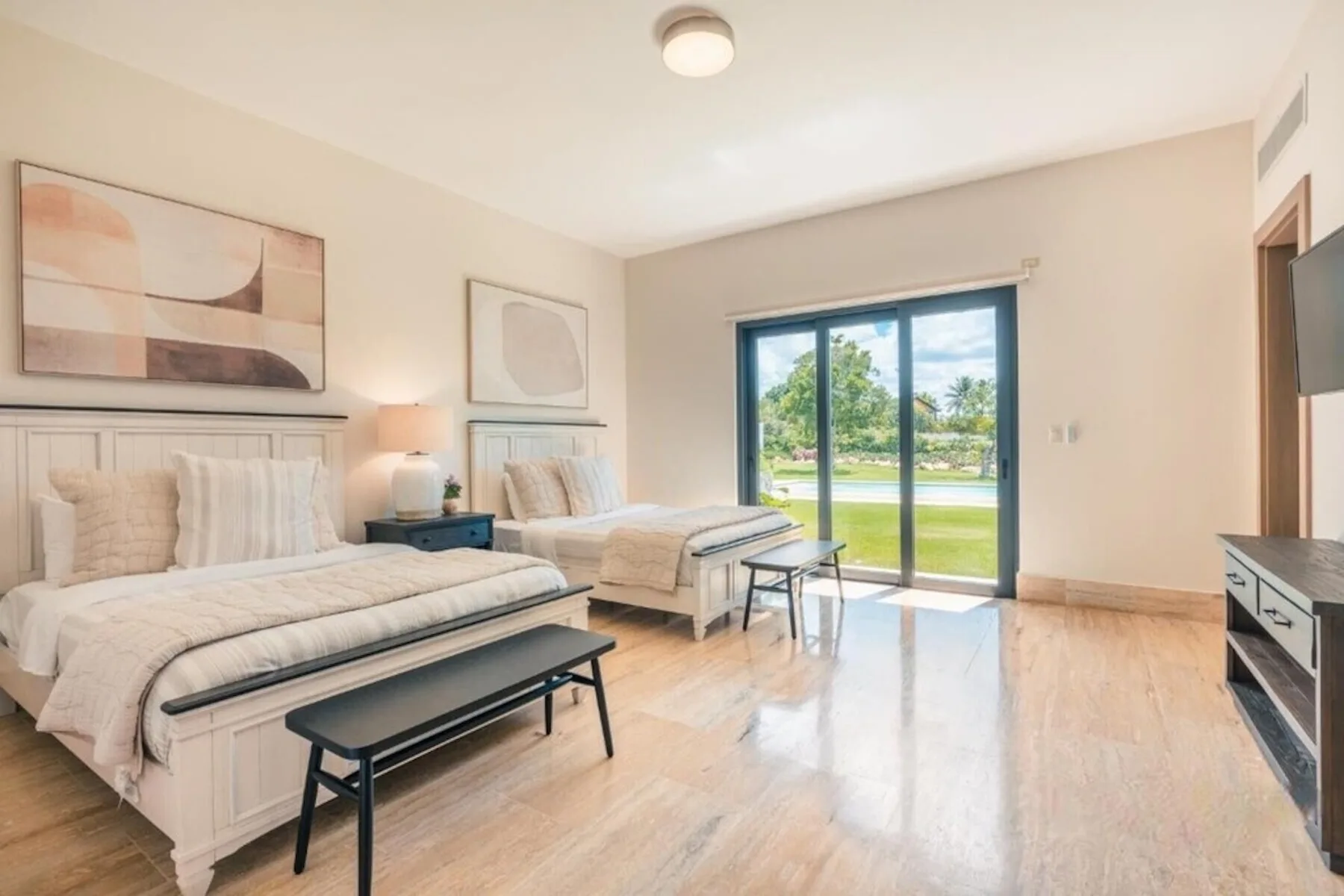 Un dormitorio luminoso con dos camas y puertas corredizas de vidrio con vistas a un césped verde.