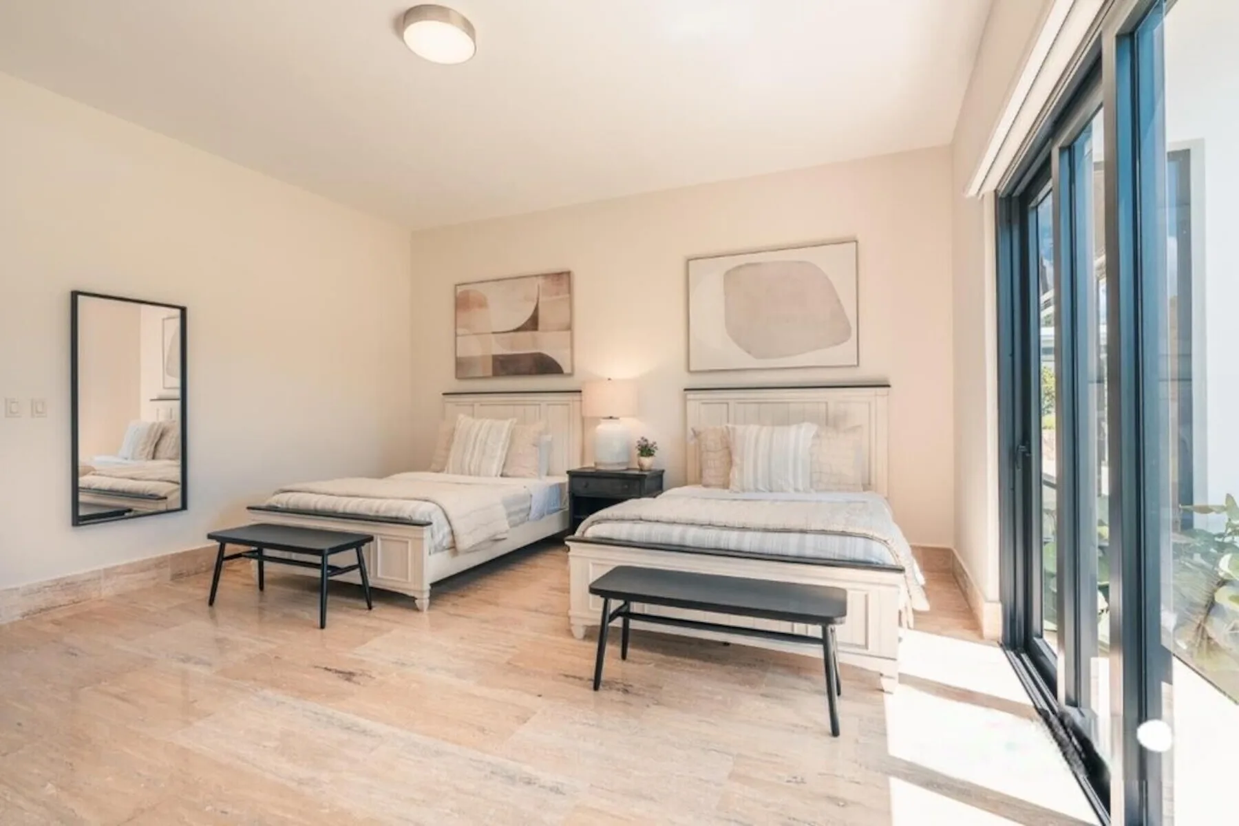 Un dormitorio luminoso con dos camas, mesitas de noche y grandes ventanas.