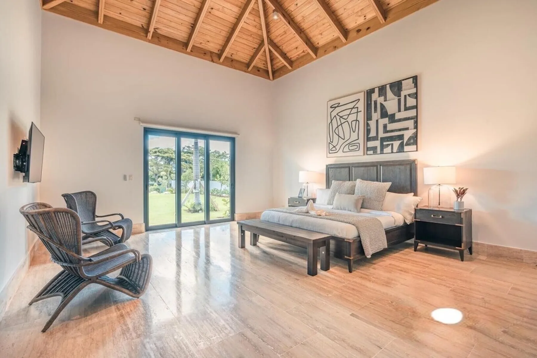 Un dormitorio luminoso con una cama grande, una zona de estar y puertas corredizas de vidrio.