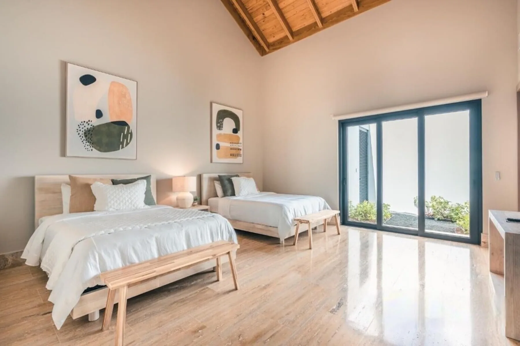 Un dormitorio luminoso con dos camas y grandes puertas de cristal junto a la vegetación.