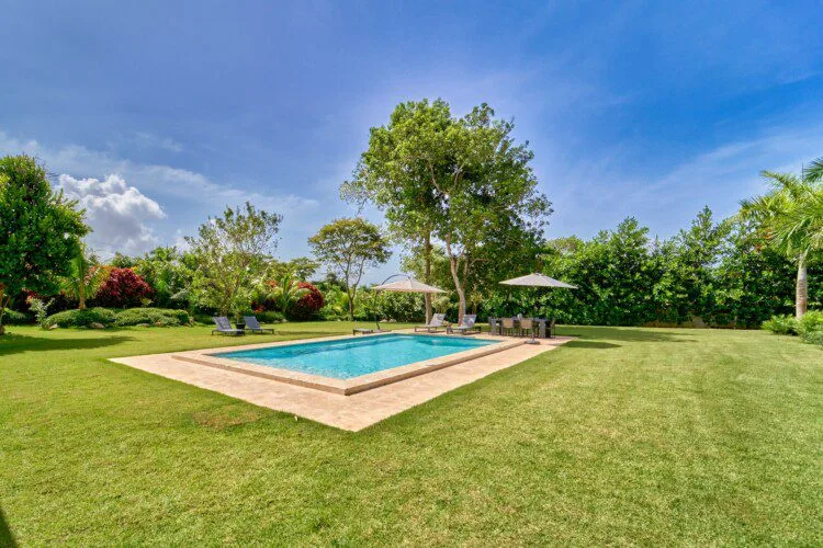 Una piscina al aire libre está rodeada de césped y un jardín paisajístico.