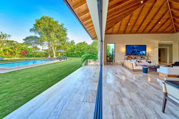 Un patio cubierto da a un césped y una piscina junto a una sala interior.
