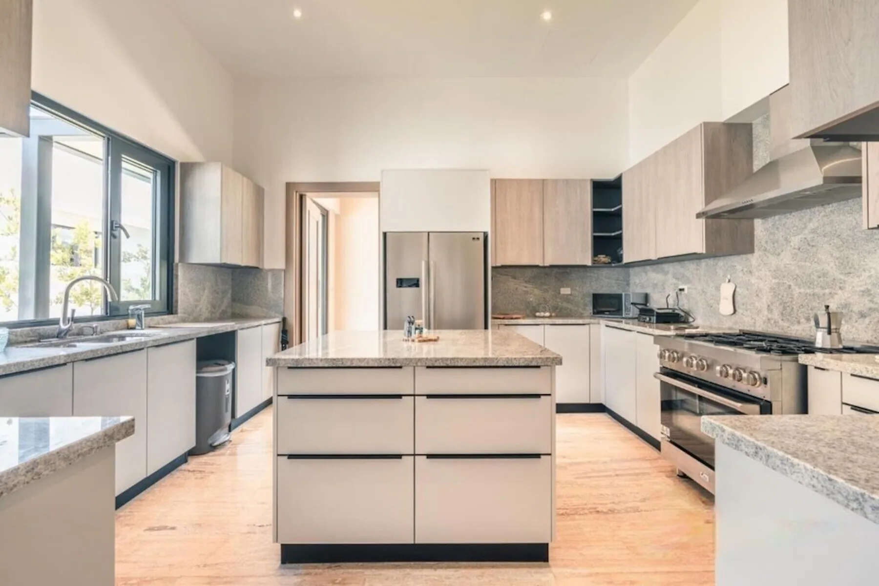 Una cocina moderna y luminosa con isla central, electrodomésticos de acero inoxidable y grandes ventanas.