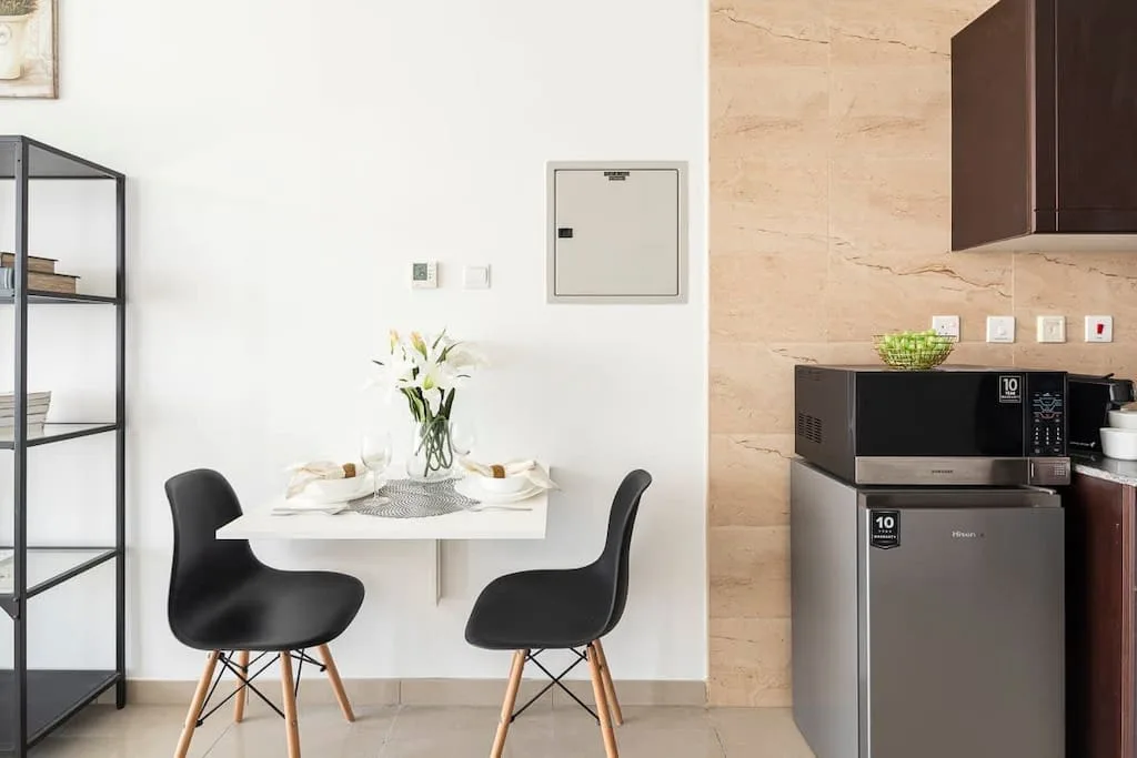 Comedor con una mesa blanca y asientos negros junto a una cocina compacta.