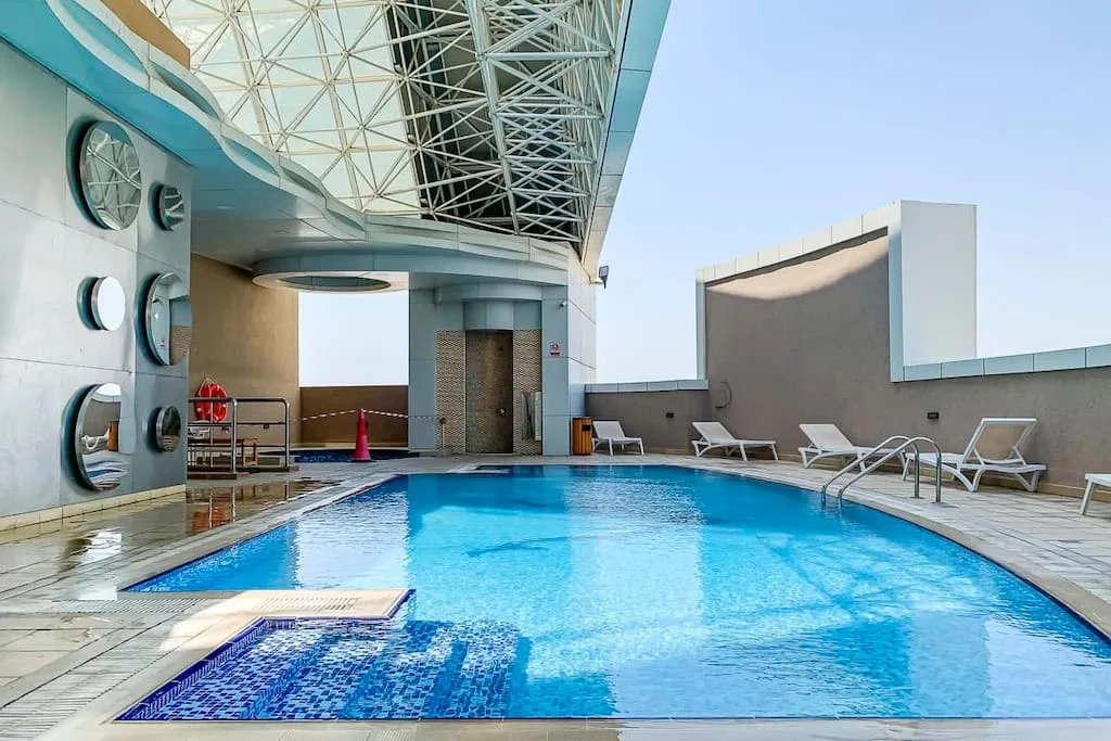 Una piscina en la azotea está junto a asientos de descanso bajo una cubierta geométrica.