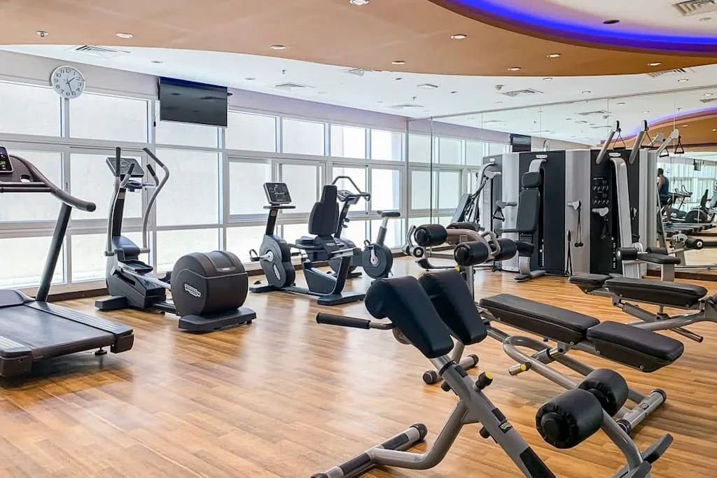 Un gimnasio con máquinas de ejercicio y equipo de pesas junto a grandes ventanales.
