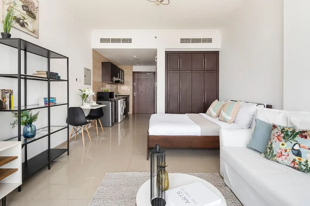 Una sala luminosa con asientos blancos, una mesa de centro y una cocina abierta.