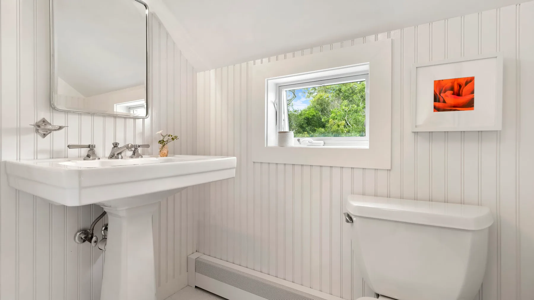 Un baño luminoso con lavabo de pedestal, inodoro y una ventana con vista a la vegetación.