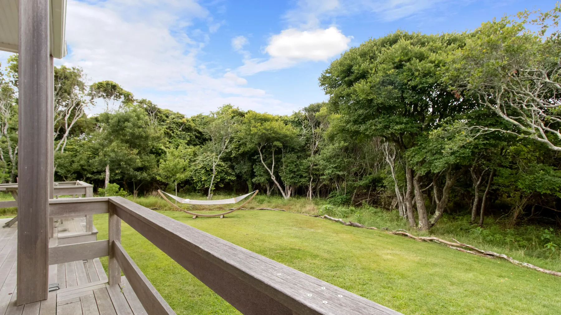 Una terraza de madera da a un césped rodeado de árboles.