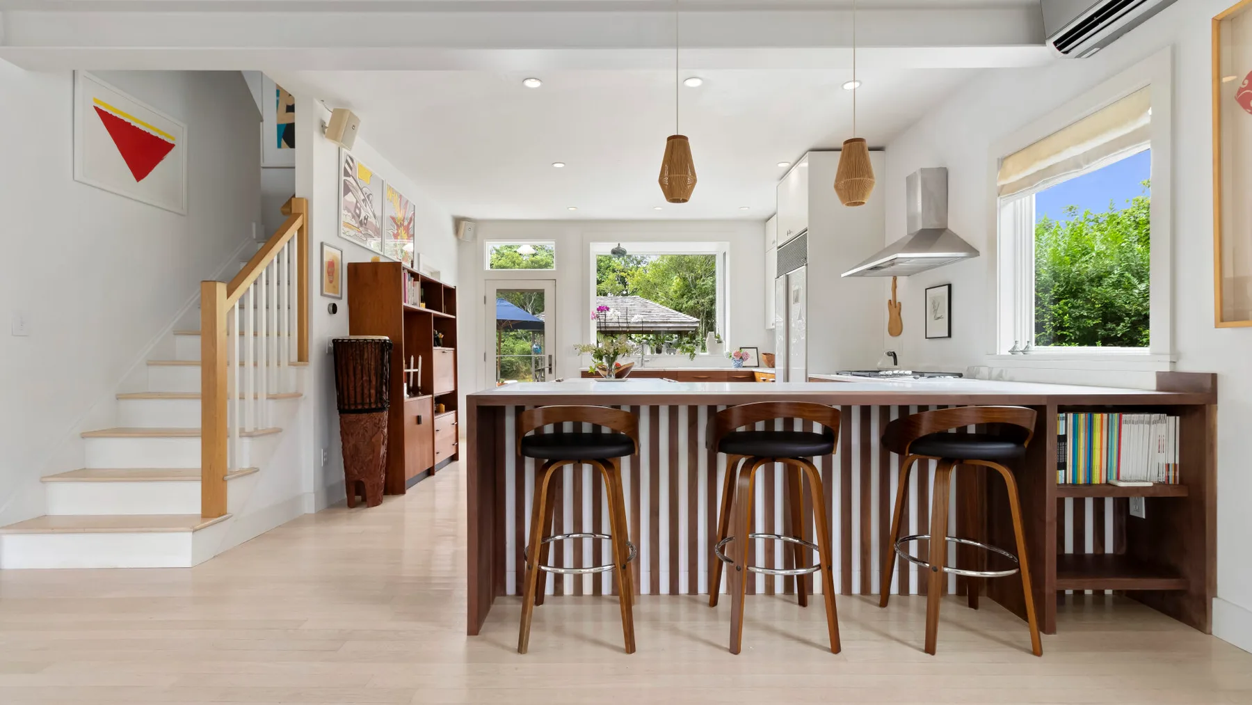 Una cocina y comedor abiertos cuentan con una barra larga de madera y taburetes.