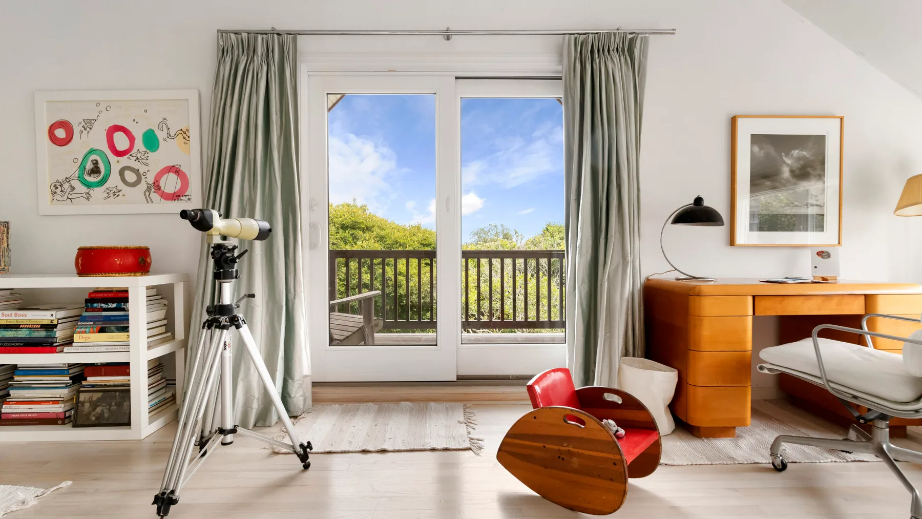 Una habitación luminosa con escritorio, asientos y puertas de vidrio que dan a un balcón.