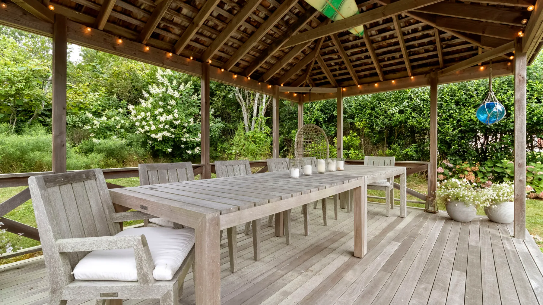 Comedor exterior cubierto con una mesa larga y vegetación alrededor.