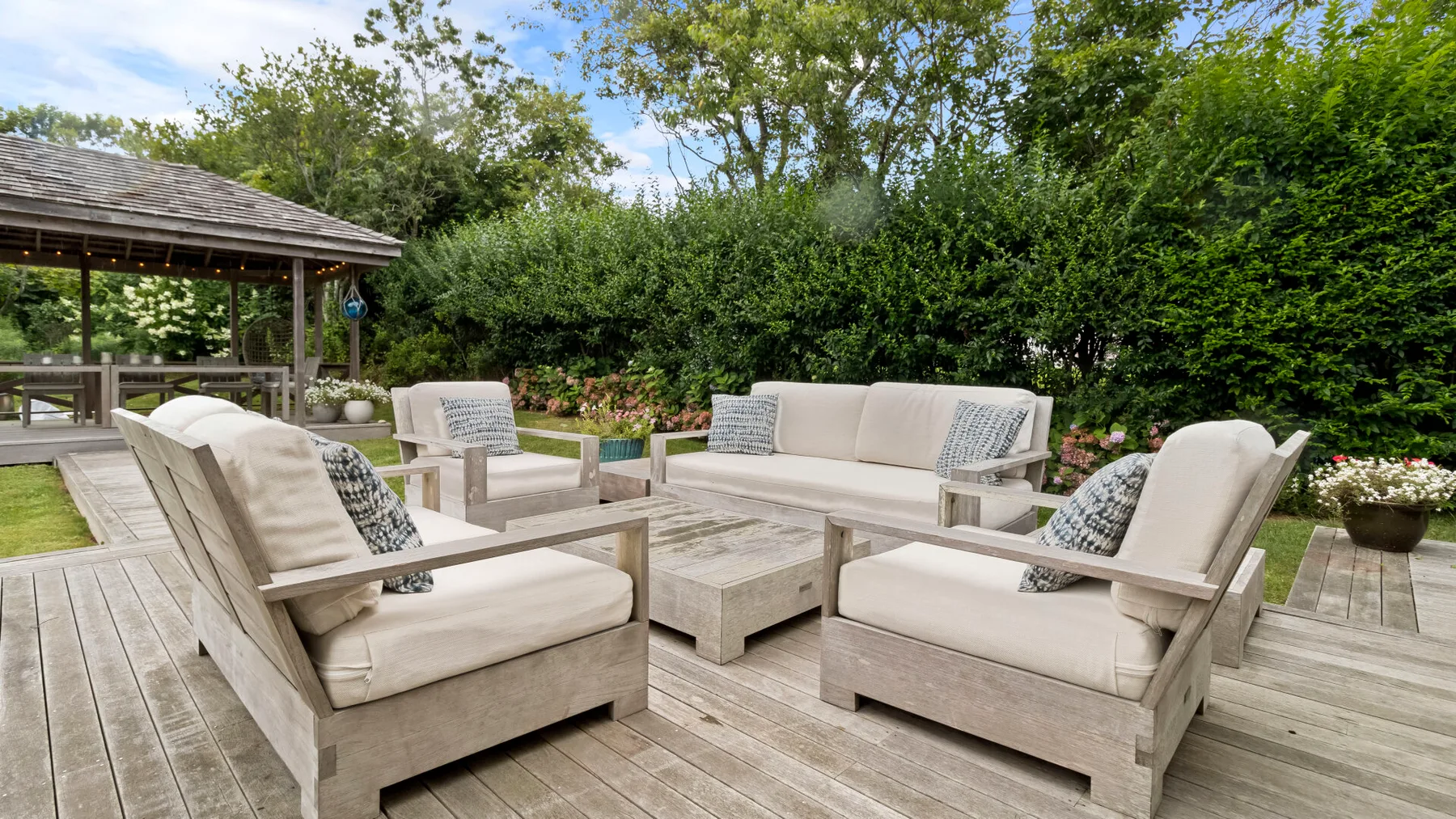Una zona de estar al aire libre con muebles acolchados está sobre una terraza de madera.