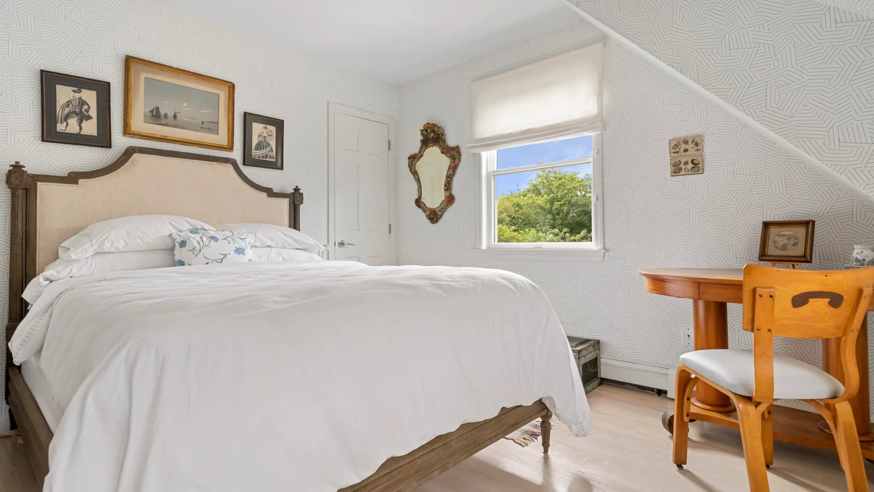 Un dormitorio con una cama tendida y una mesa de madera junto a la ventana.