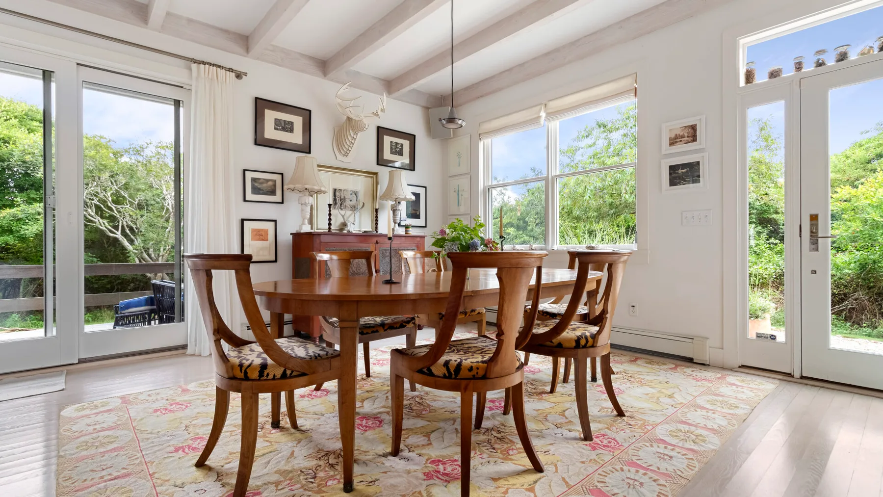 Un comedor con una mesa de madera y sillas junto a grandes ventanales.