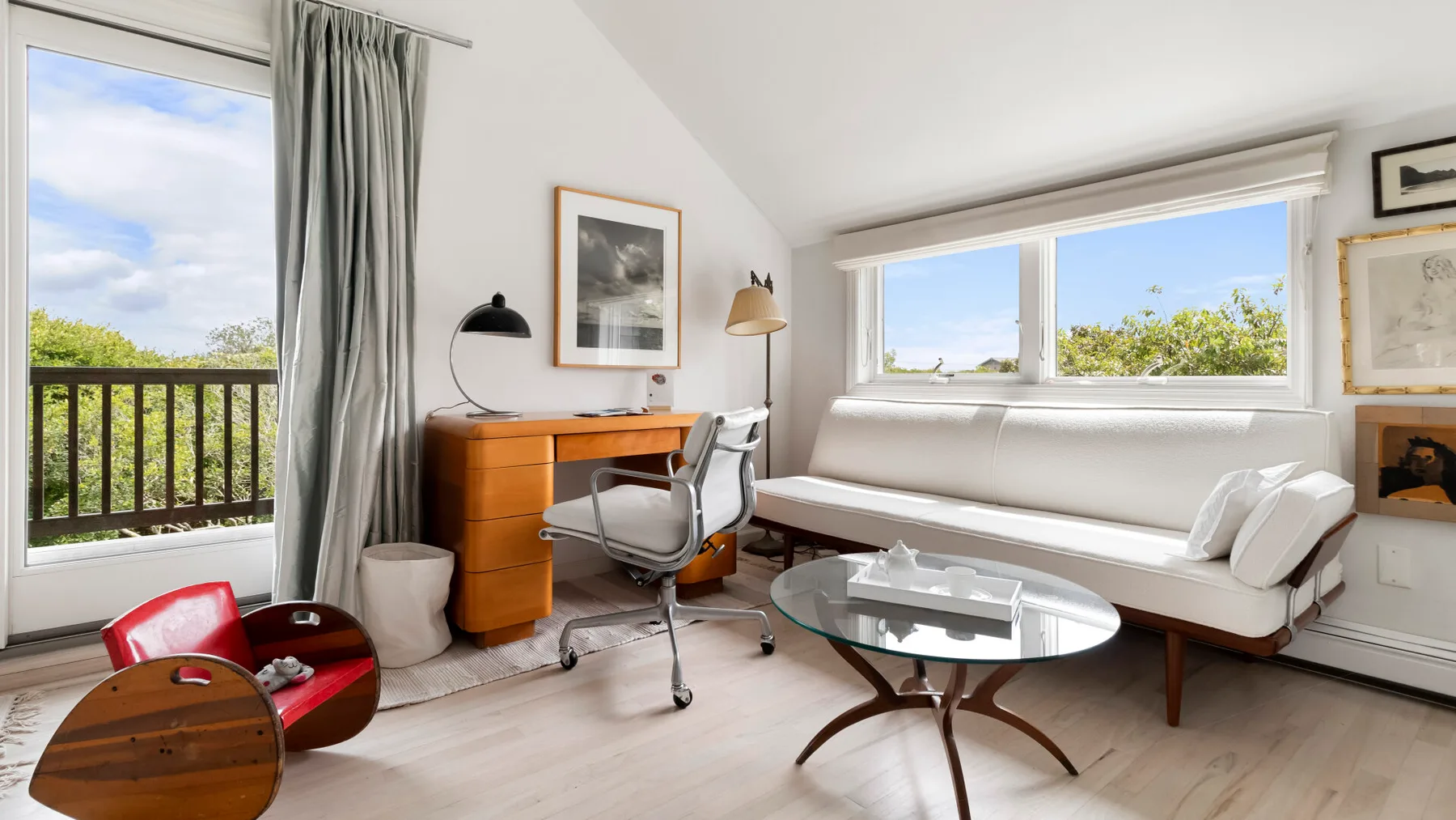 Una habitación luminosa con escritorio, asientos y grandes ventanas con vistas a la vegetación.