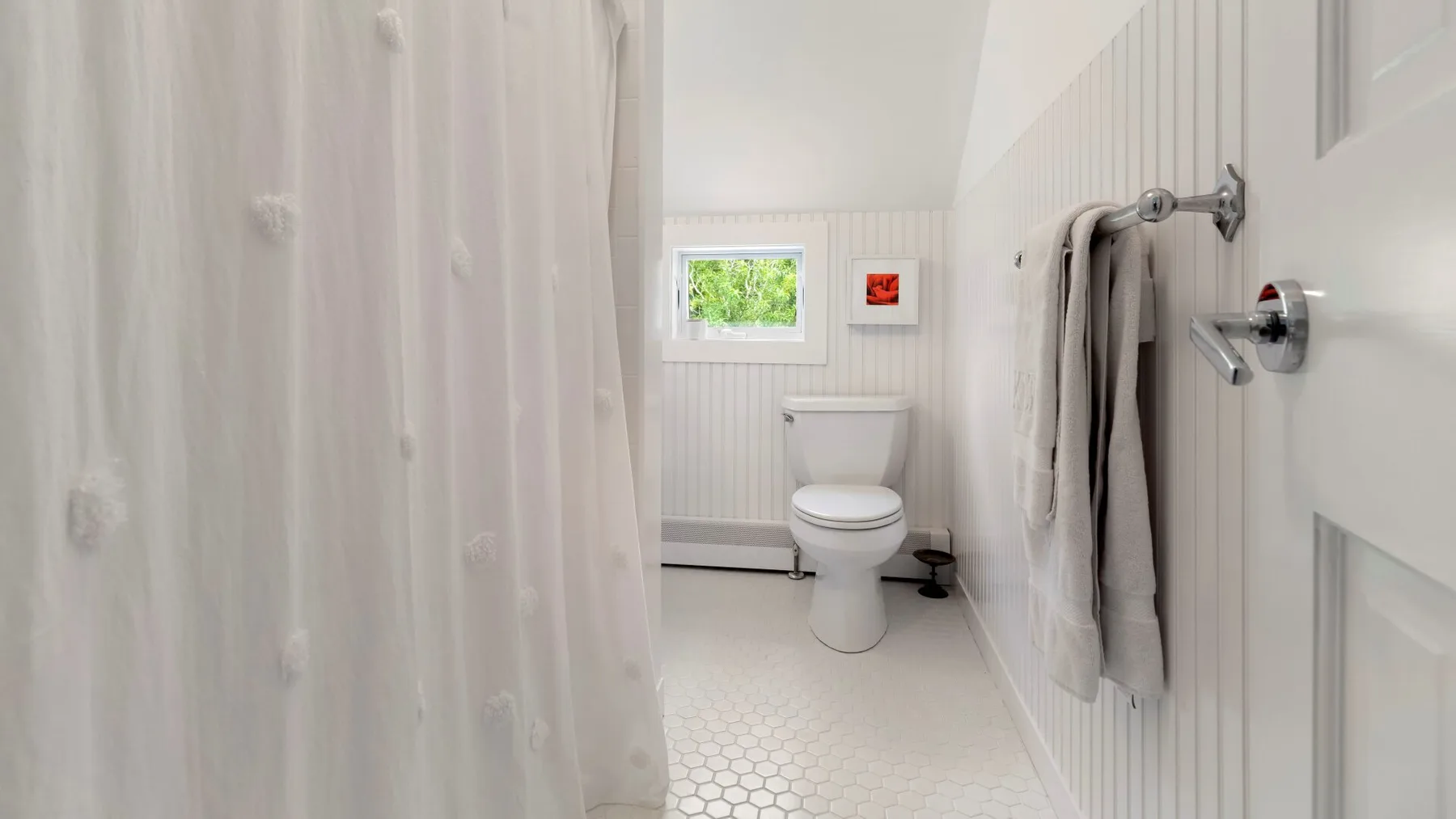 Un baño luminoso con inodoro, cortina de ducha y toallas colgadas en la pared.