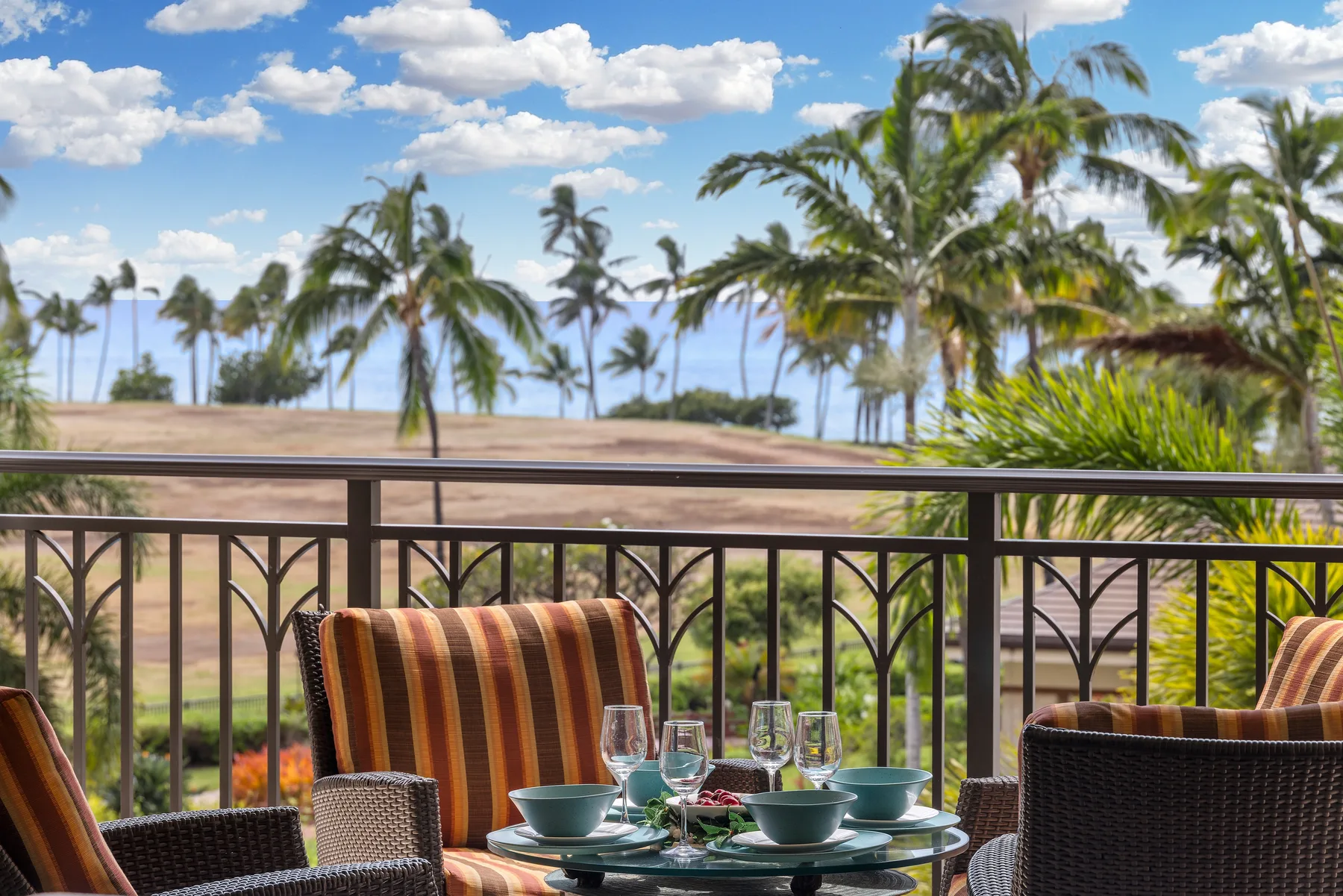 Outdoor seating overlooks palm trees and the ocean beyond a metal railing.