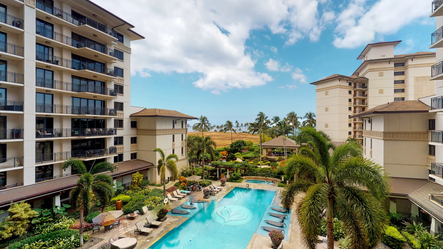 A swimming pool sits among landscaped gardens between several apartment buildings.