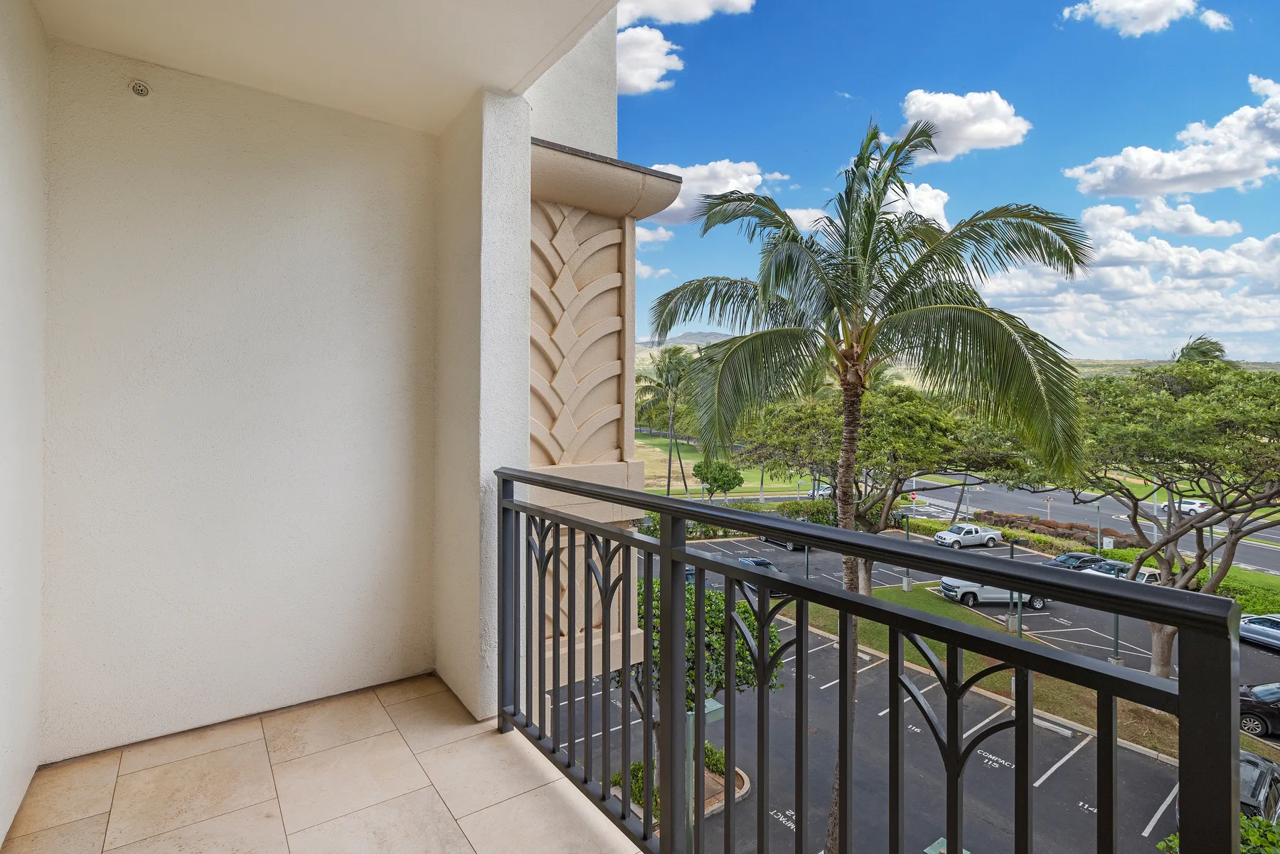 A tiled balcony overlooks palm trees and a parking lot under a blue sky.