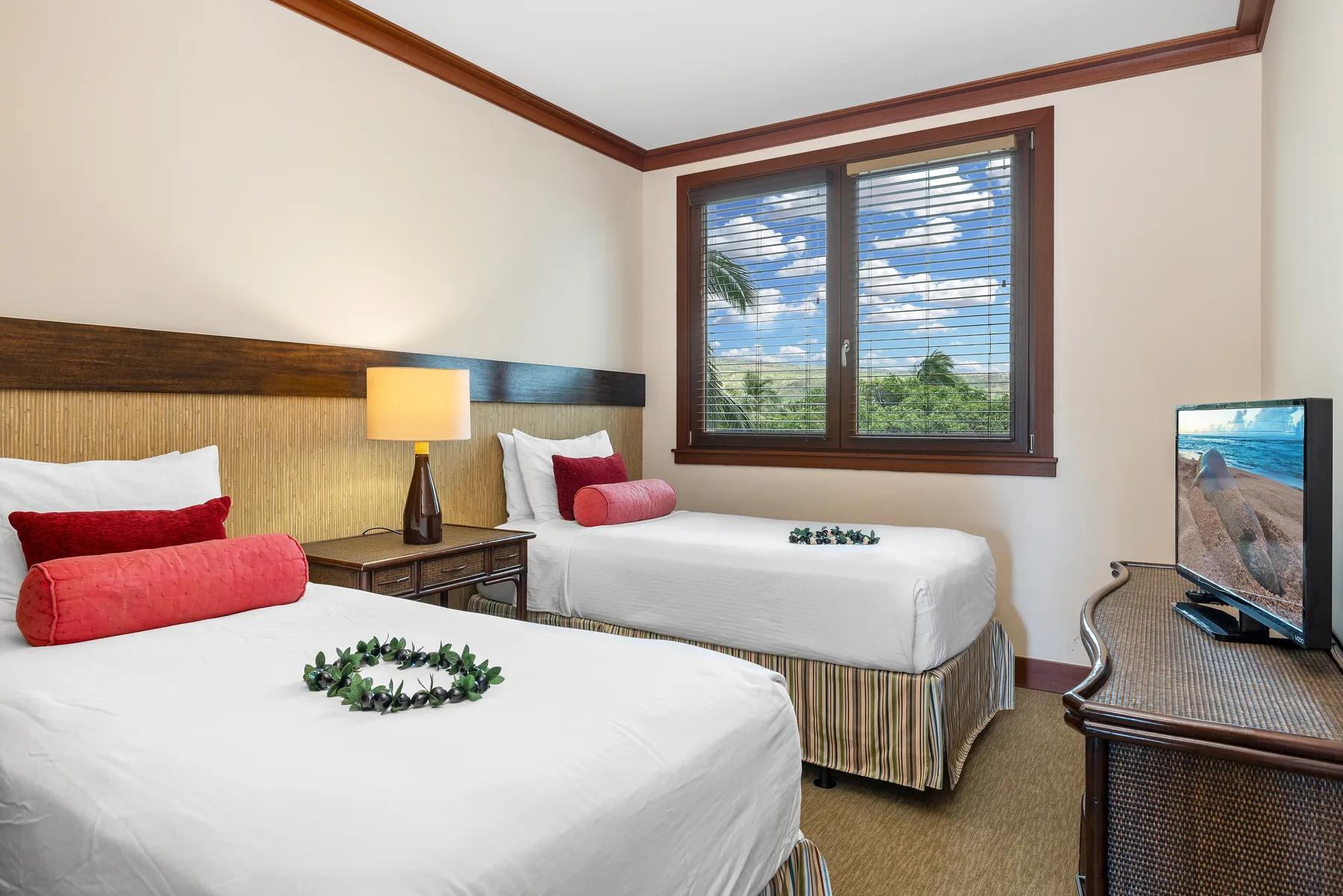 A bedroom with two beds and a window overlooking greenery.