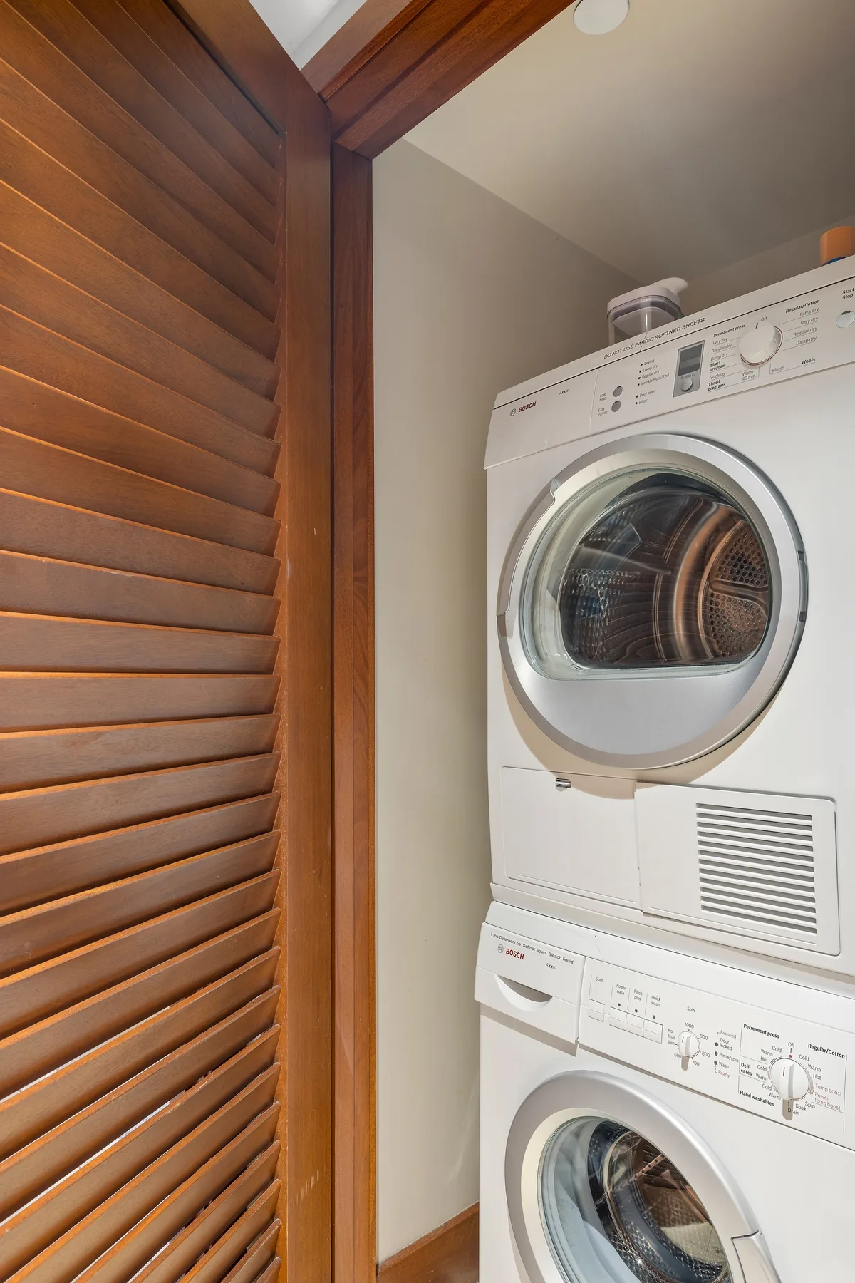 A laundry area with stacked washer and dryer beside a wooden louvered door.