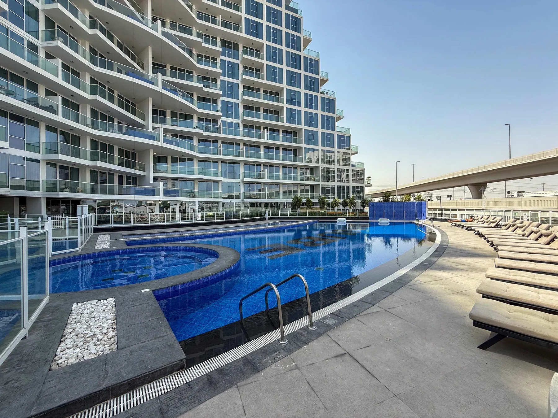 Una piscina al aire libre junto a un edificio moderno y filas de asientos reclinables.