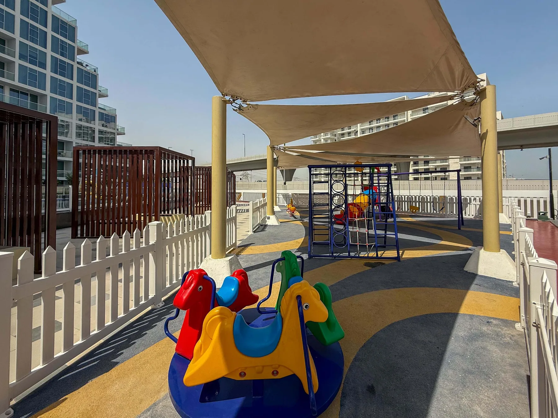 Un patio de juegos al aire libre con equipos coloridos bajo grandes toldos.
