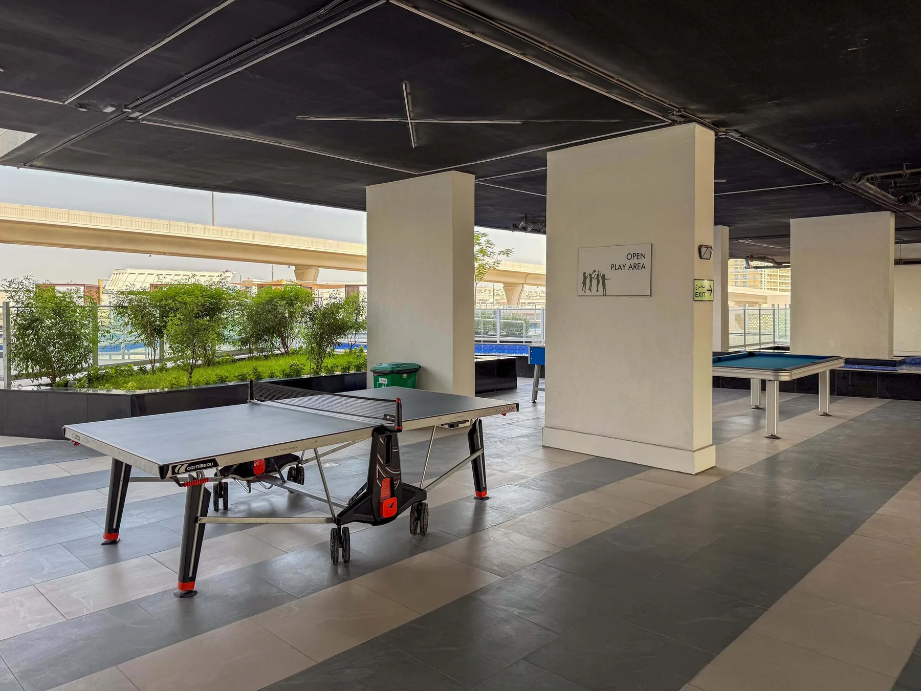 Un área recreativa cubierta con mesas de ping-pong y una fila de ventanas.