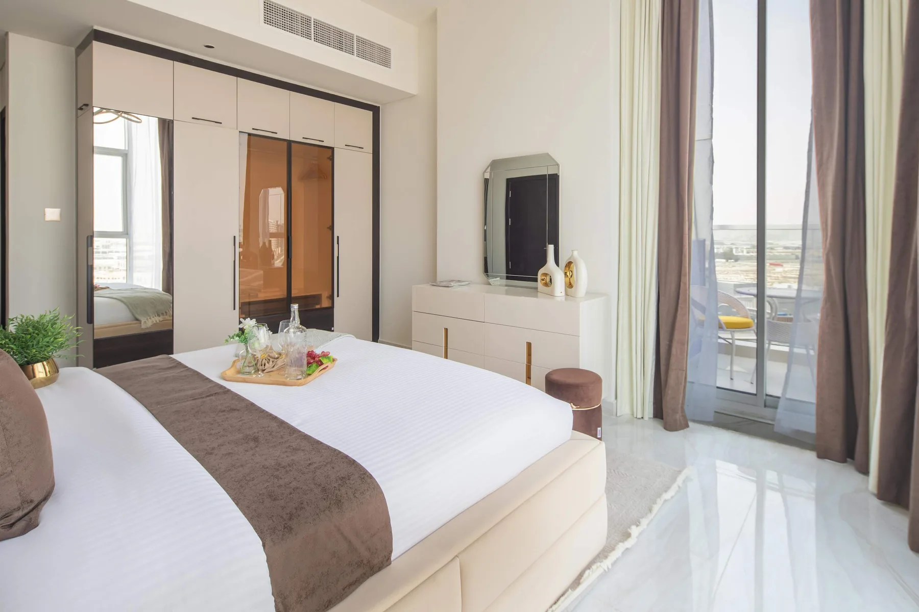Un dormitorio luminoso con ropa de cama blanca y ventanas altas que dan a un balcón.
