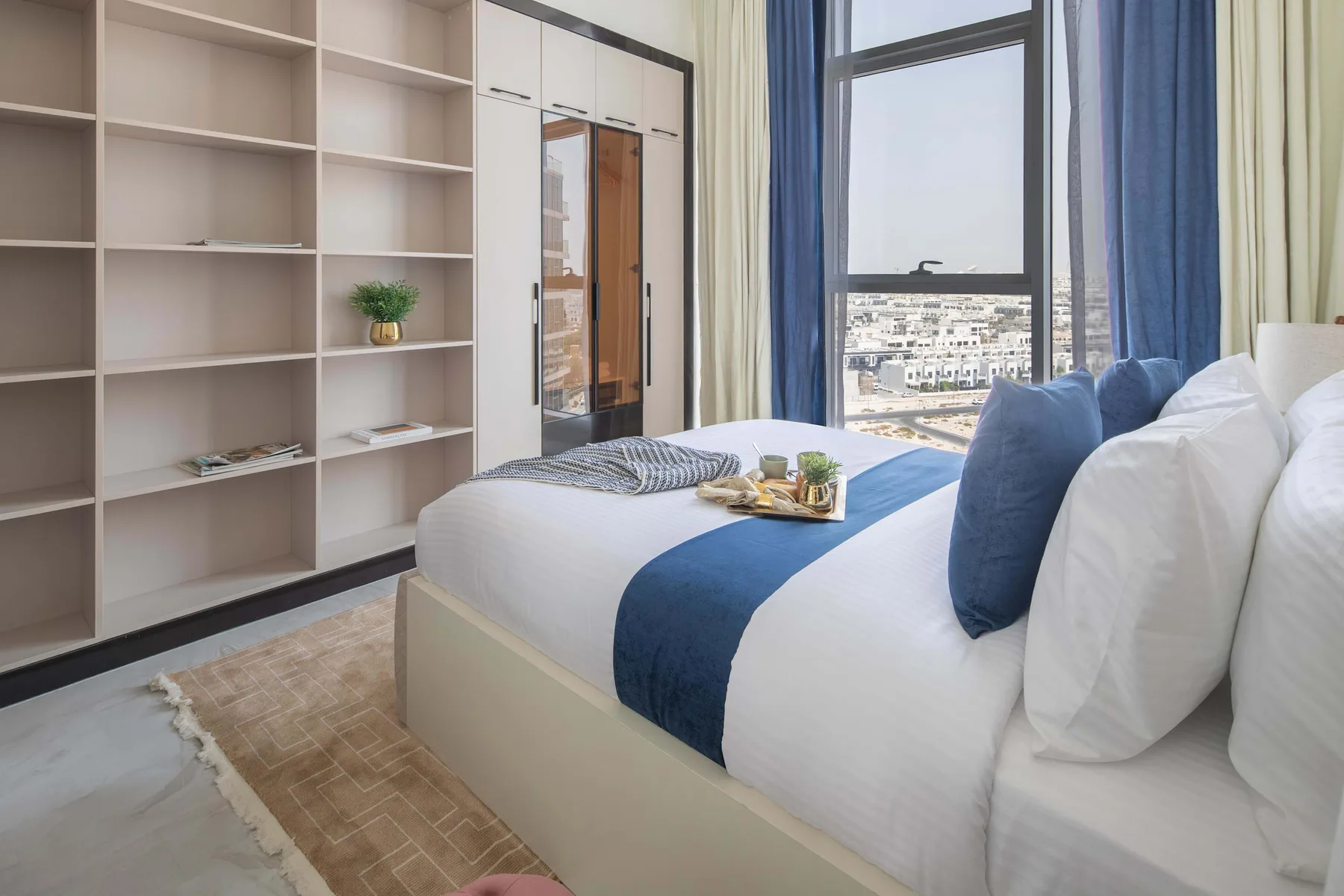 Un dormitorio luminoso con una cama bien hecha y estanterías empotradas junto a la ventana.