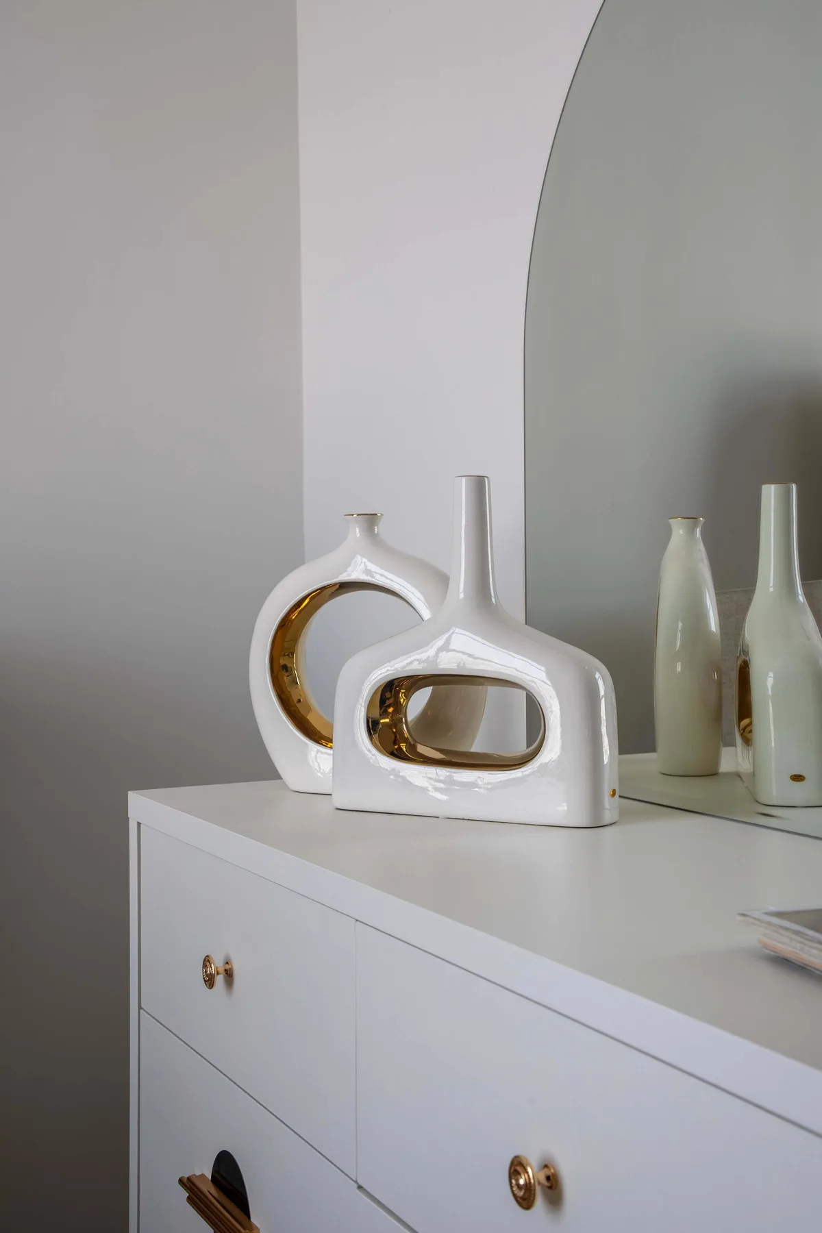 Una cómoda blanca exhibe jarrones decorativos de cerámica junto a un espejo alto.