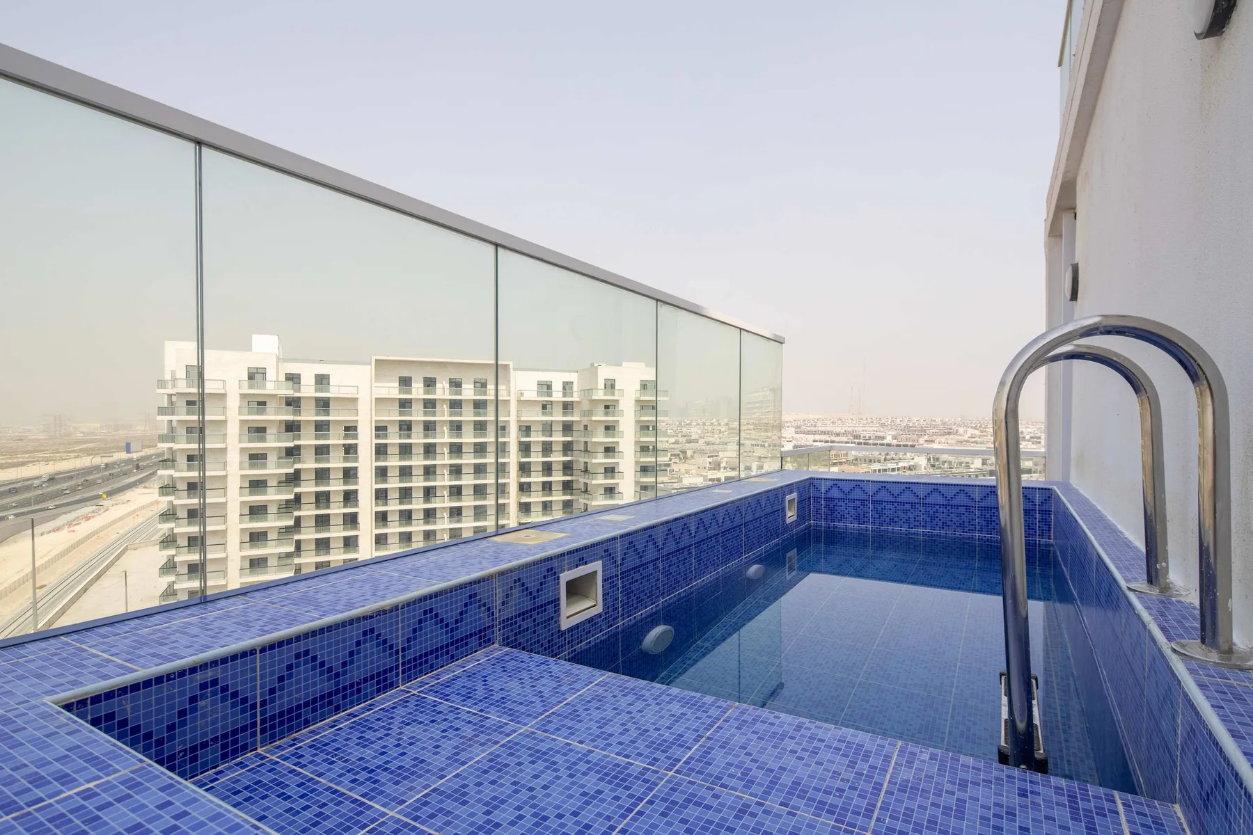Una piscina en la azotea con azulejos azules da a edificios cercanos.