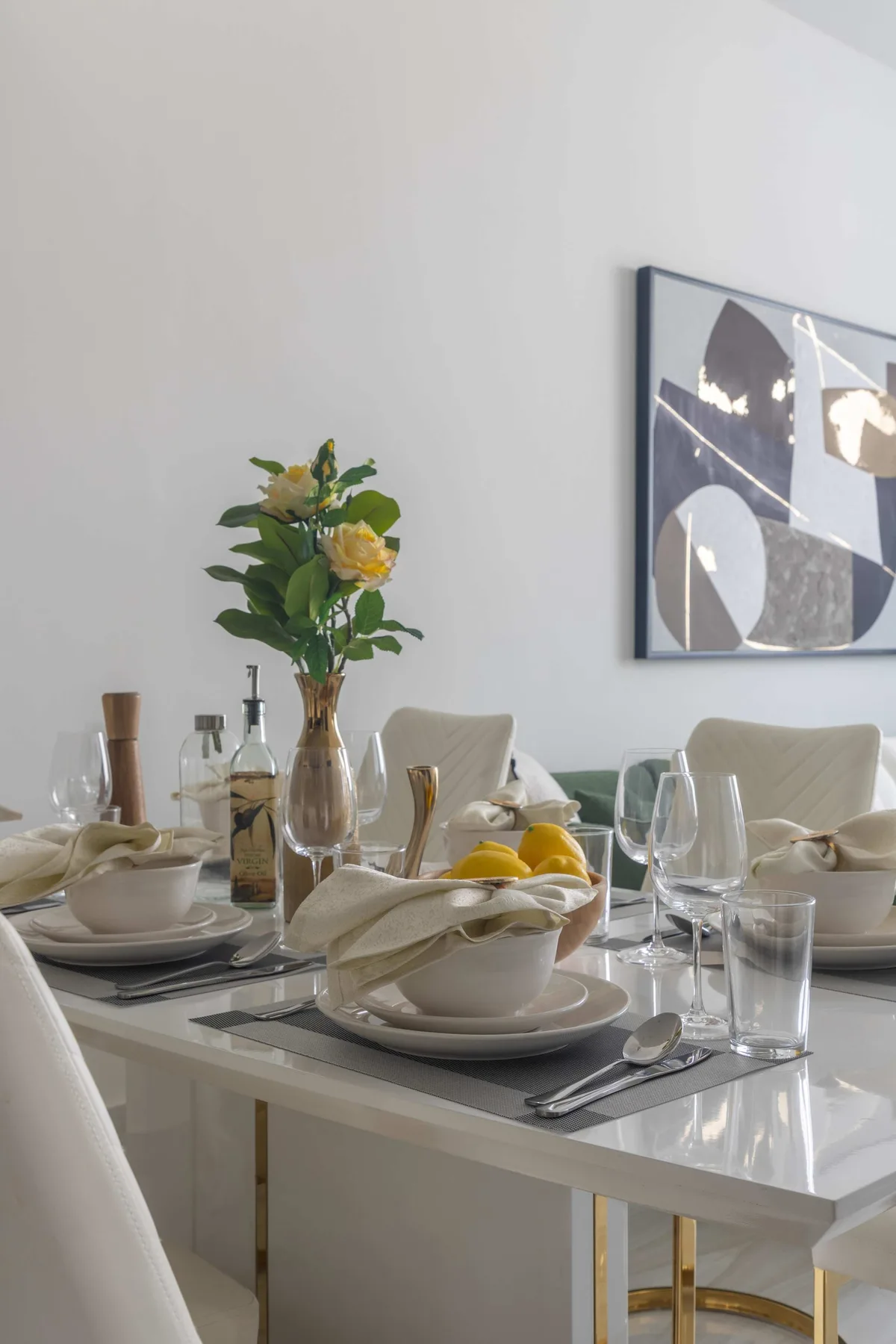 Una mesa de comedor está preparada con platos, cristalería, servilletas dobladas y un arreglo floral.