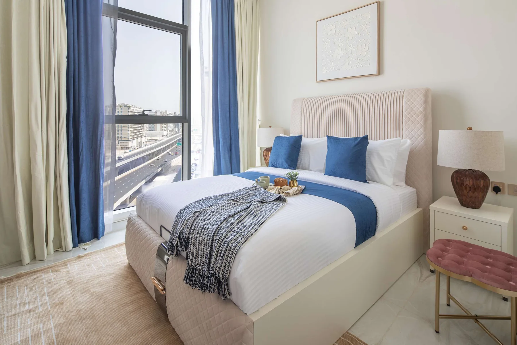 Un dormitorio luminoso con una cama bien hecha junto a una ventana grande.