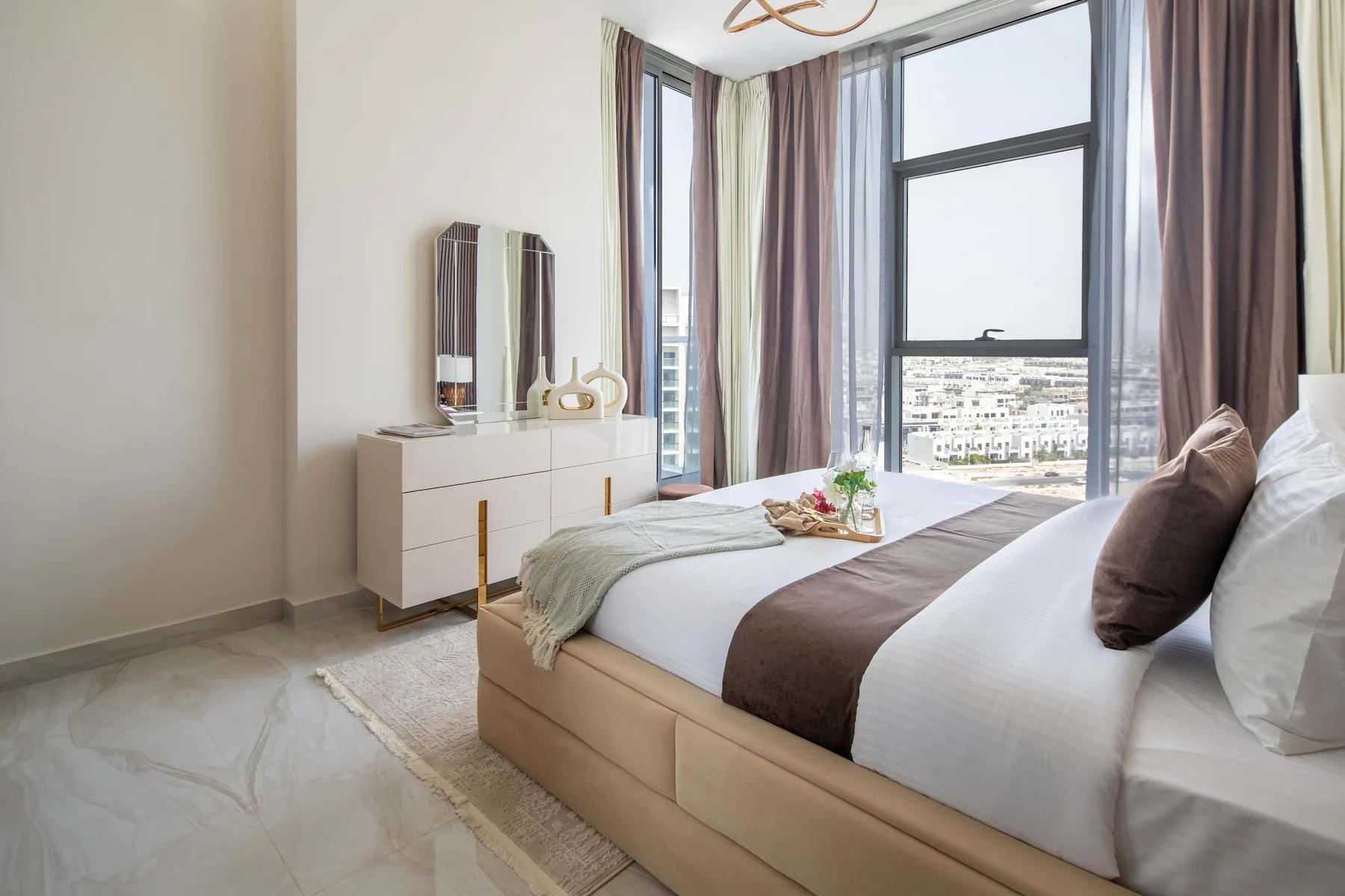 Un dormitorio luminoso con una cama junto a ventanas altas con cortinas.