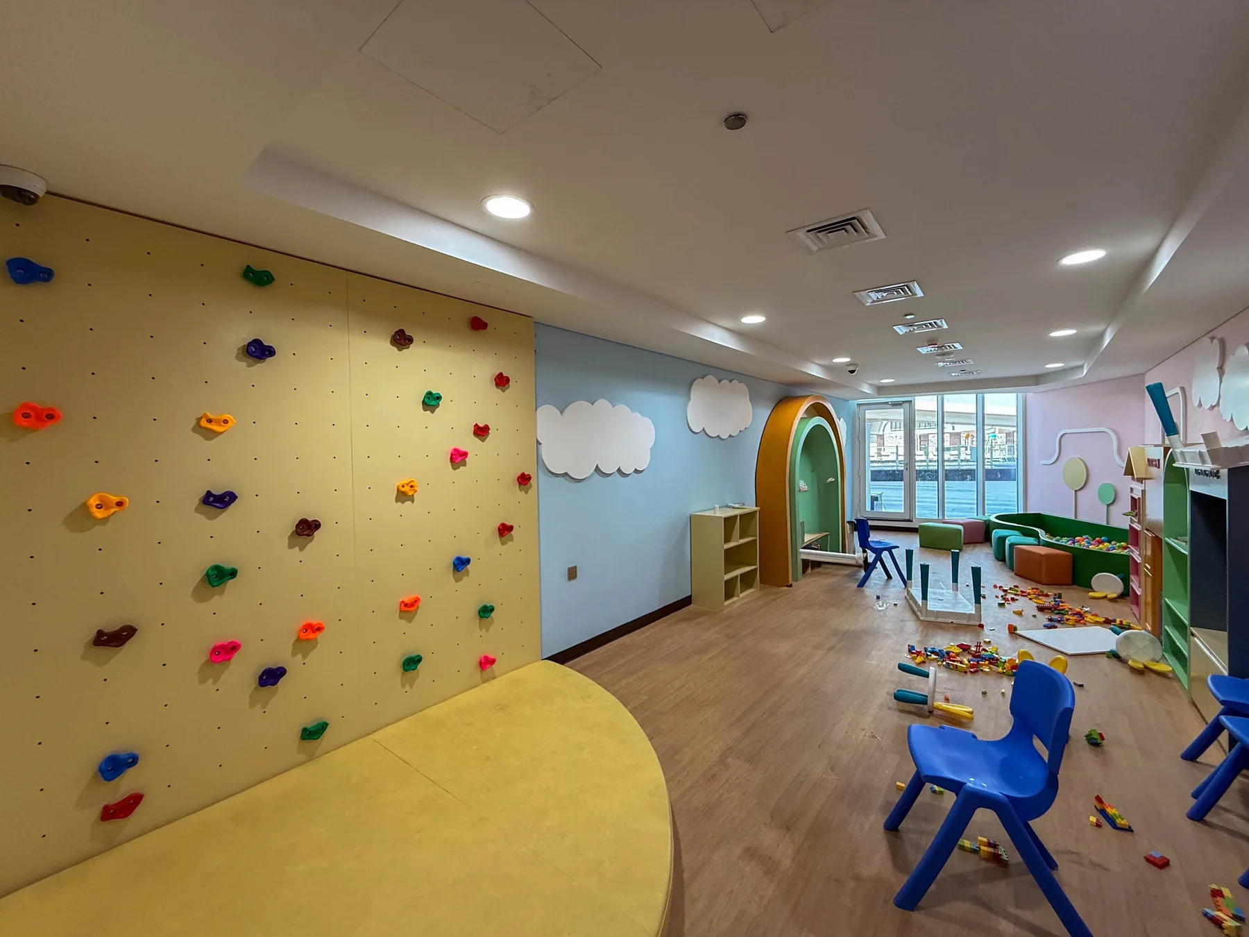 Una colorida sala de juegos interior tiene un muro para escalar, sillas infantiles y juguetes esparcidos.