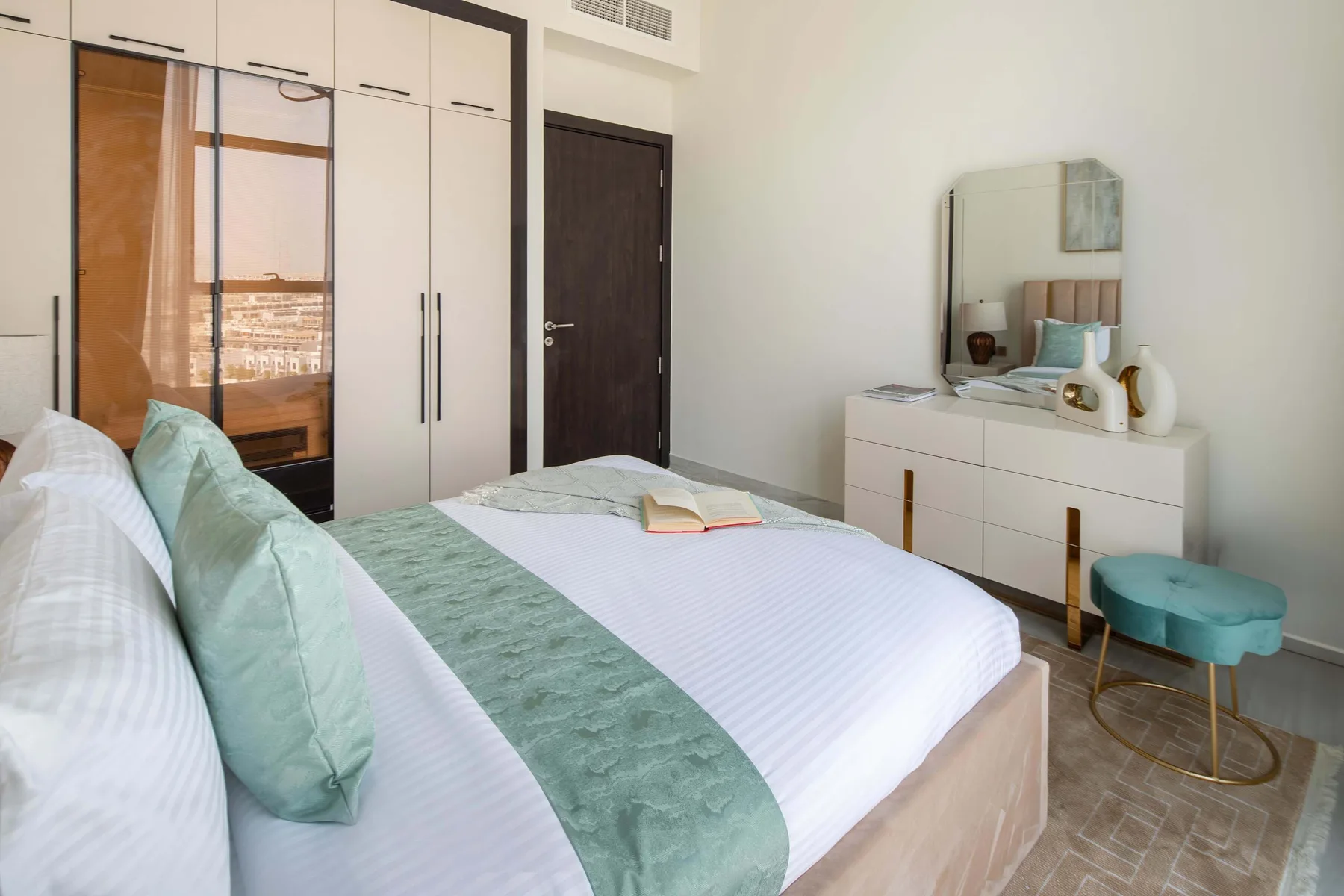 Un dormitorio con una cama bien tendida, ropa de cama verde claro y una cómoda con espejo.