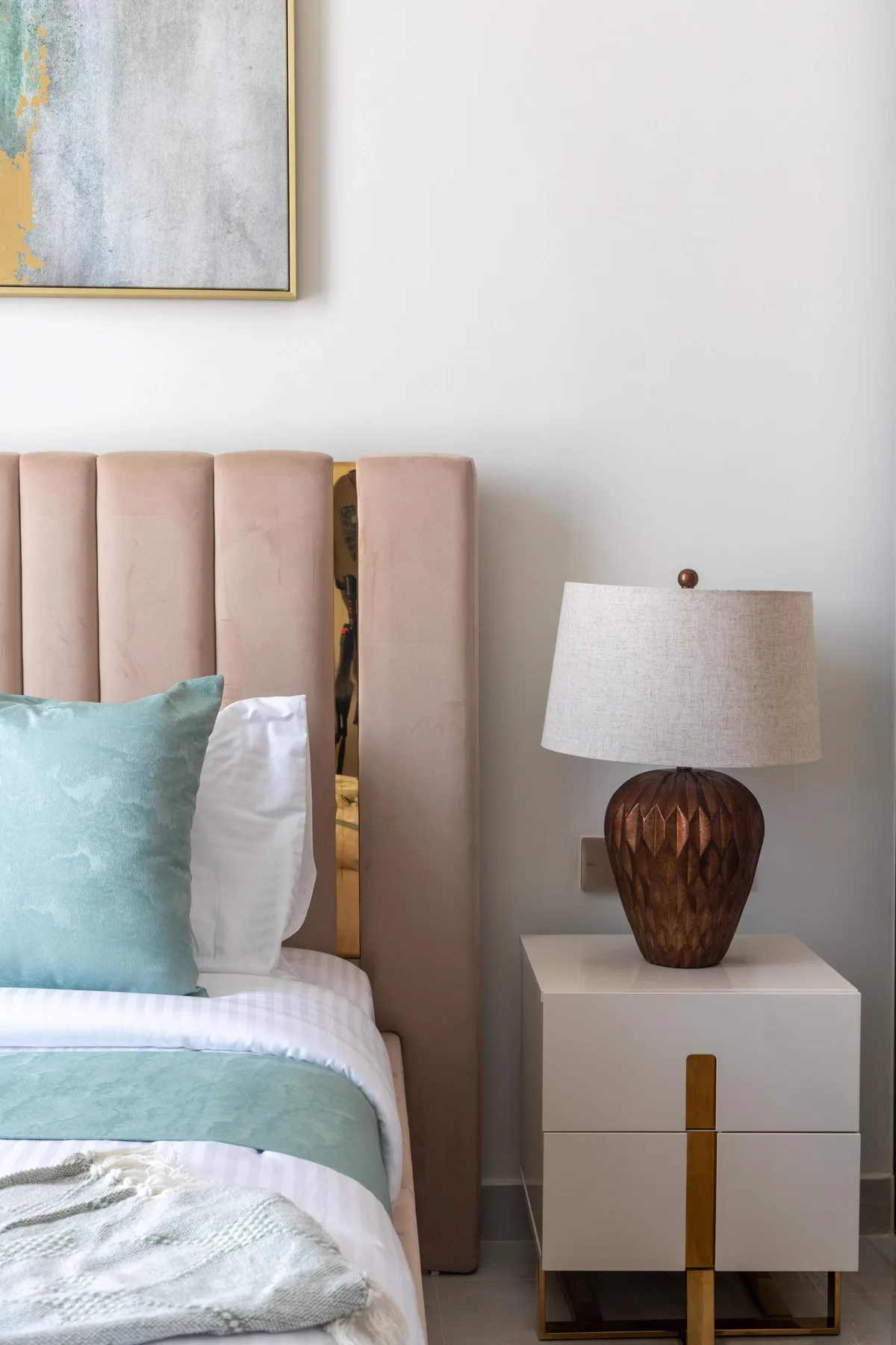 Un dormitorio con cama, cabecero tapizado claro y mesita de noche.