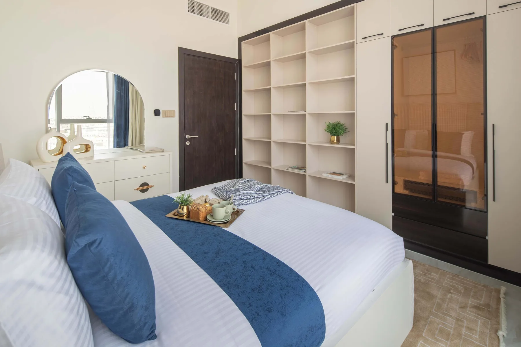Un dormitorio con una cama tendida y estanterías empotradas.