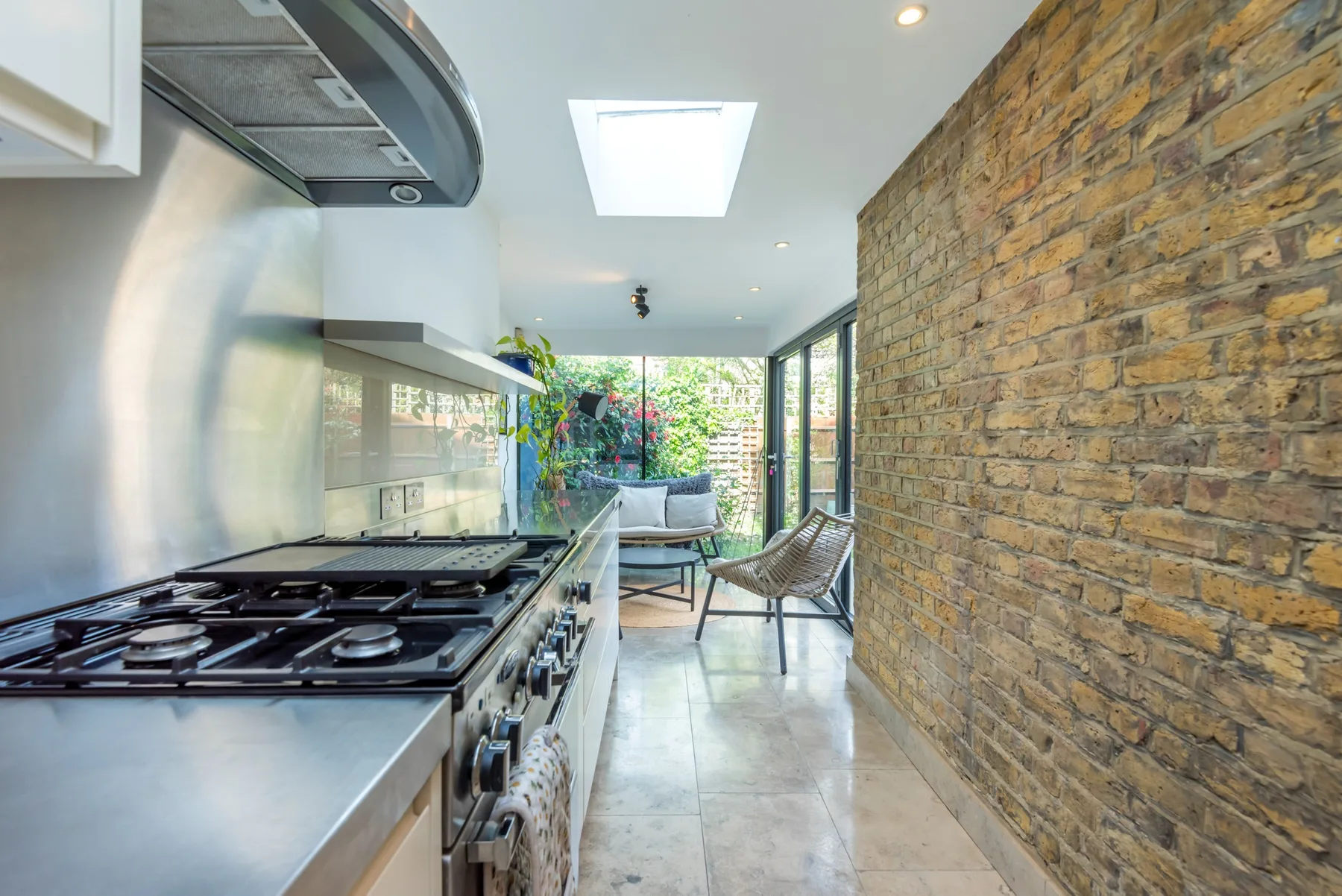 A narrow kitchen opens onto a seating area beside a brick wall.