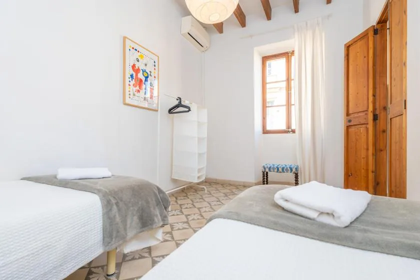 A bright bedroom with two beds, a window, and wooden wardrobes.