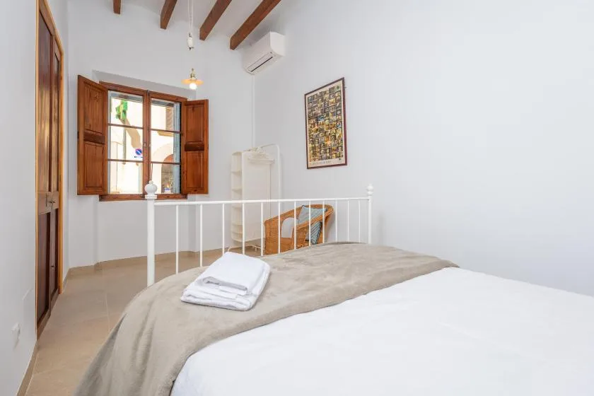 A bright bedroom with a bed, wooden window, and exposed ceiling beams.