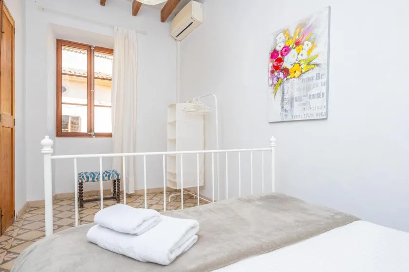 A bright bedroom with a bed, folded towels, and a window.