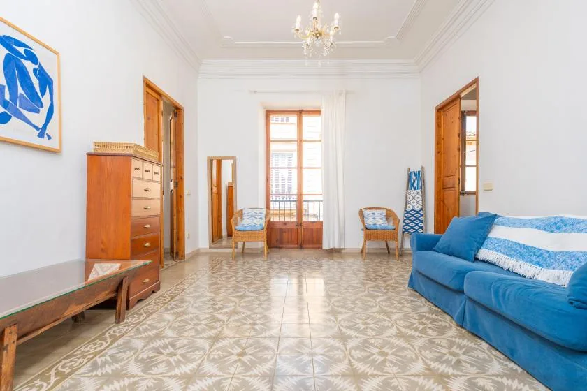 A bright living room with blue seating and patterned tile flooring.