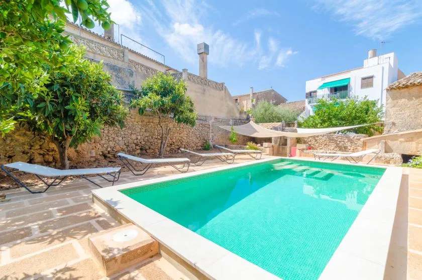 A sunny outdoor swimming pool is surrounded by stone walls and greenery.