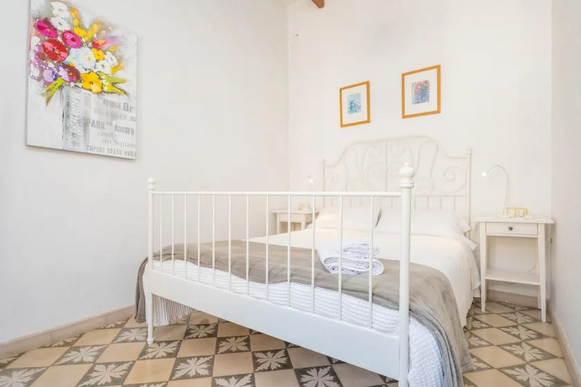 A bright bedroom with a white metal bed and floral artwork on the wall.